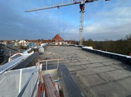 Bautenstand 07.04.2026: Auf der Baustelle sind in den vergangenen Wochen erneut deutliche Fortschritte erzielt worden. Die wesentlichen Rohbauarbeiten sind bereits abgeschlossen – das Gebäude ist vollständig errichtet und durch den Einbau von Fenstern und Haustüren nun klar in seiner finalen Kubatur erkennbar. Im Bereich Dach konnten die vorbereitenden Maßnahmen erfolgreich fertiggestellt werden. Der Fokus liegt derzeit auf der Abdichtung des Hauptdachs, die planmäßig umgesetzt wird. Auch der technische Ausbau entwickelt sich kontinuierlich weiter: Die Elektroinstallation sowie die Gewerke Heizung, Sanitär und Lüftung befinden sich in einem fortgeschrittenen Stadium und werden aktuell in den oberen Etagen weitergeführt. Der Innenausbau nimmt ebenfalls zunehmend Gestalt an. Große Teile des Trockenbaus sind bereits realisiert, einzelne Wandbereiche geschlossen. Die Kellerdämmung befindet sich in den letzten Zügen, und die Montage der Stahlzargen ist abgeschlossen. Die Estricharbeiten wurden im Kellergeschoss erfolgreich beendet und schreiten im Erdgeschoss weiter voran. Parallel dazu haben die Fassadenarbeiten begonnen, sodass sich auch das äußere Erscheinungsbild des Gebäudes weiterentwickelt. Fazit: Der Baufortschritt verläuft weiterhin stabil und im vorgesehenen Zeitrahmen.